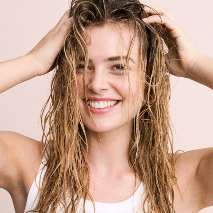 Vrouw met nat haar die glimlacht en een natuurlijke glans en gezonde uitstraling van het haar toont.