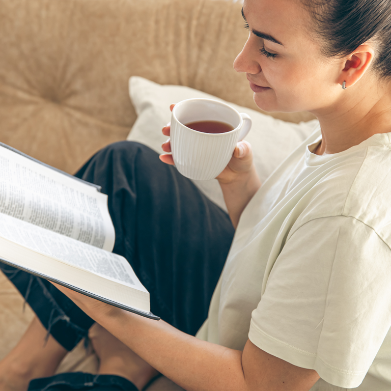 A woman reading a book while drinking tea